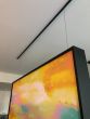 A framed artwork is suspended from a black Xpo Rail Track installed on the ceiling.